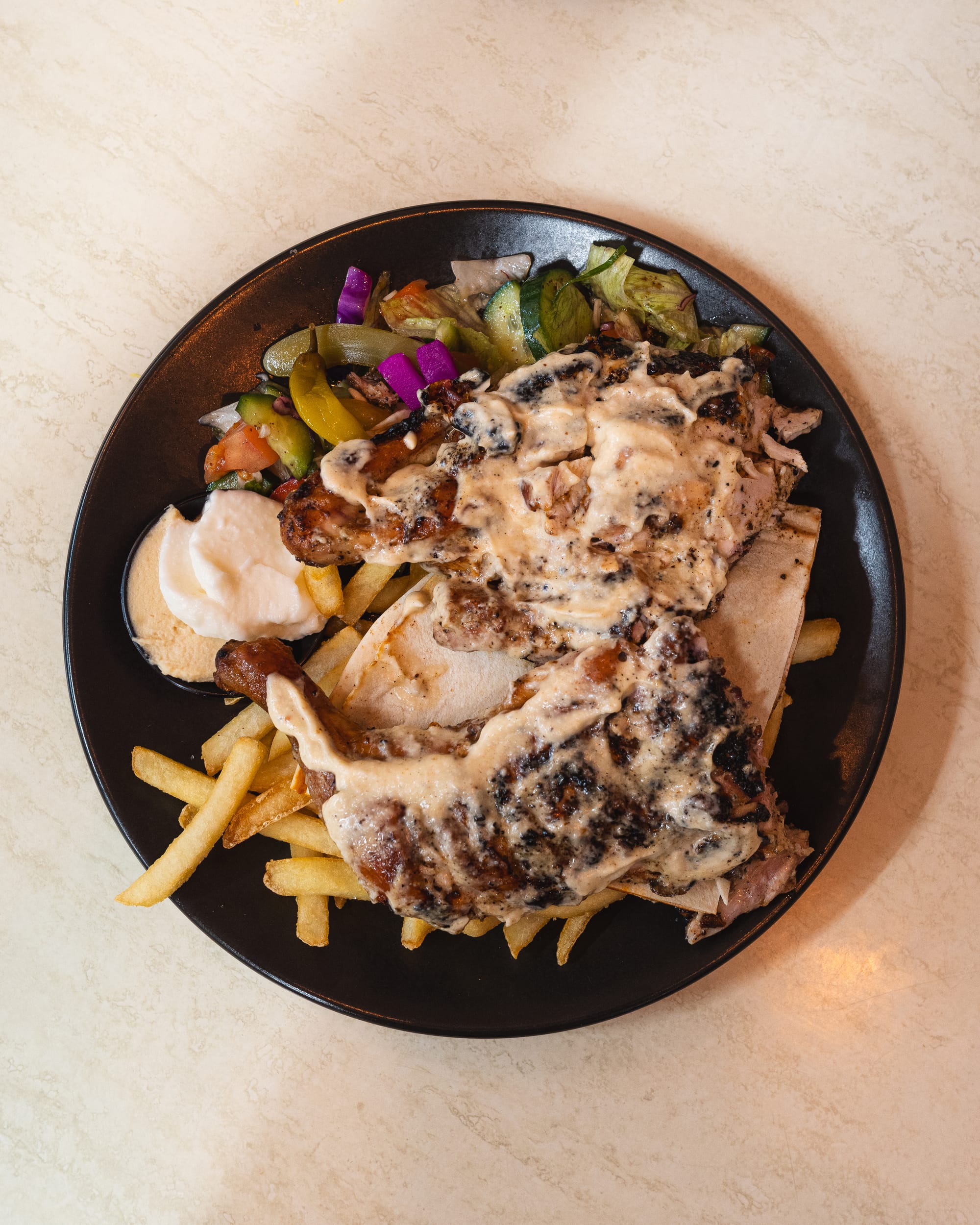 Top down shot of charcoal chicken with hummus, garlic dip, chips and salad
