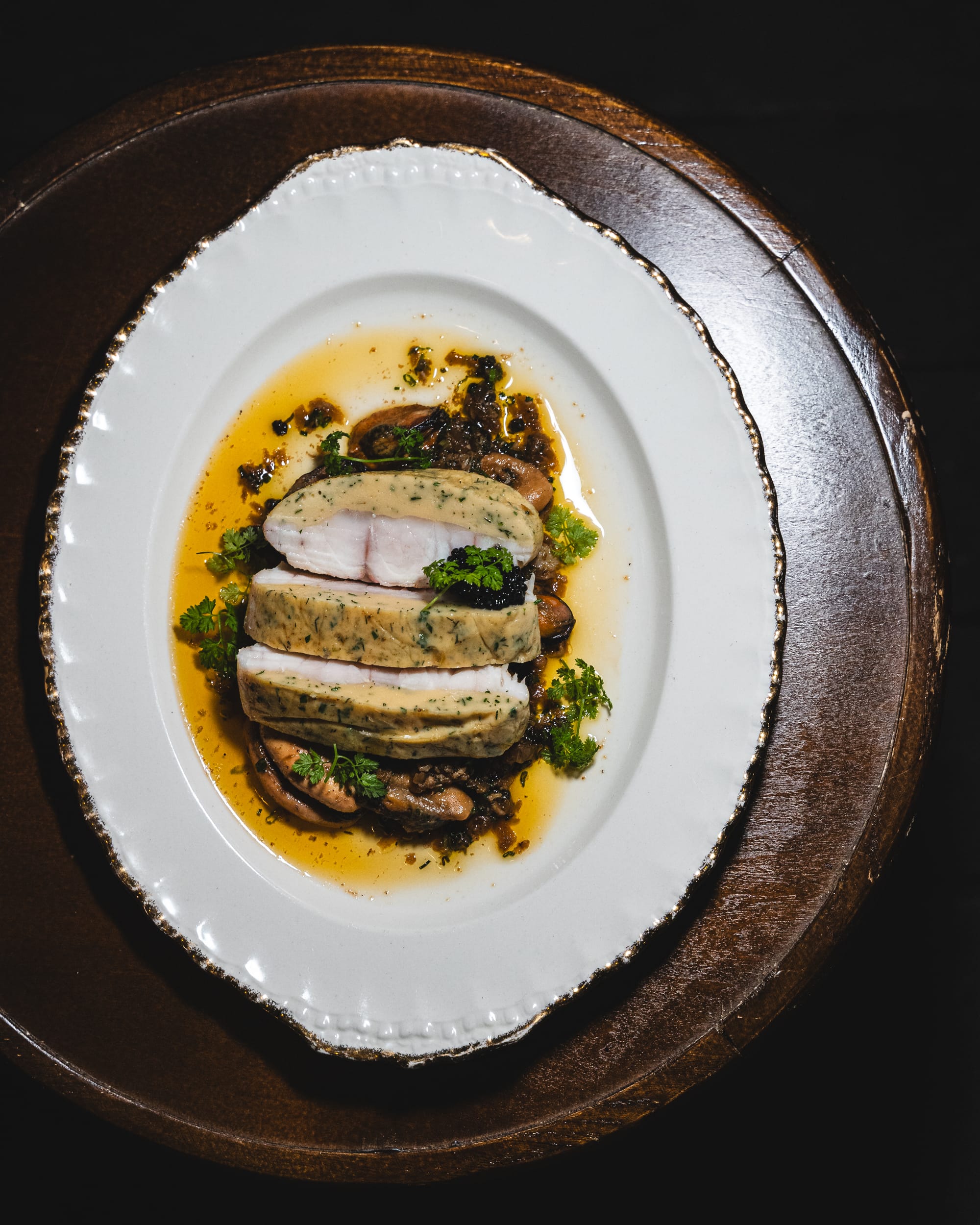 Top down shot of fish ballotine with flavoured oiled drizzled around it, topped with caviar and parsley
