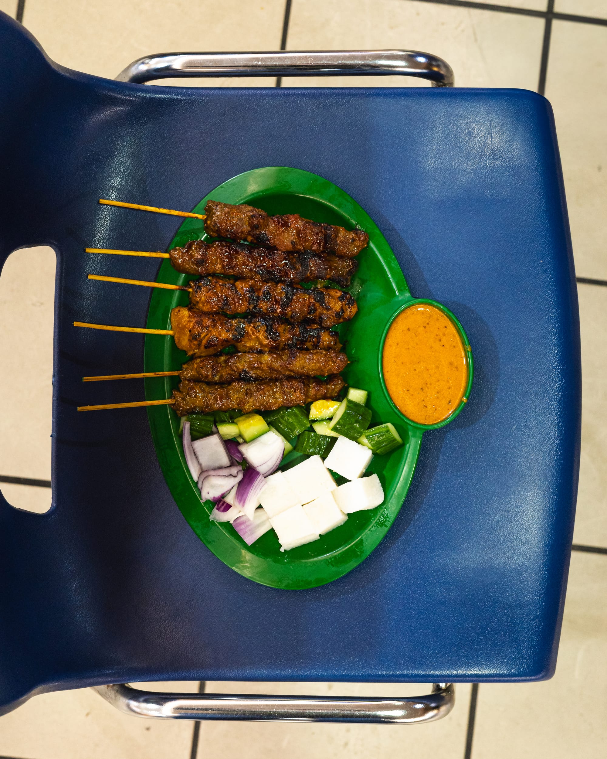 Top down shot of grilled satay skewers with peanut sauce, chopped cucumber and red onion and compressed rice