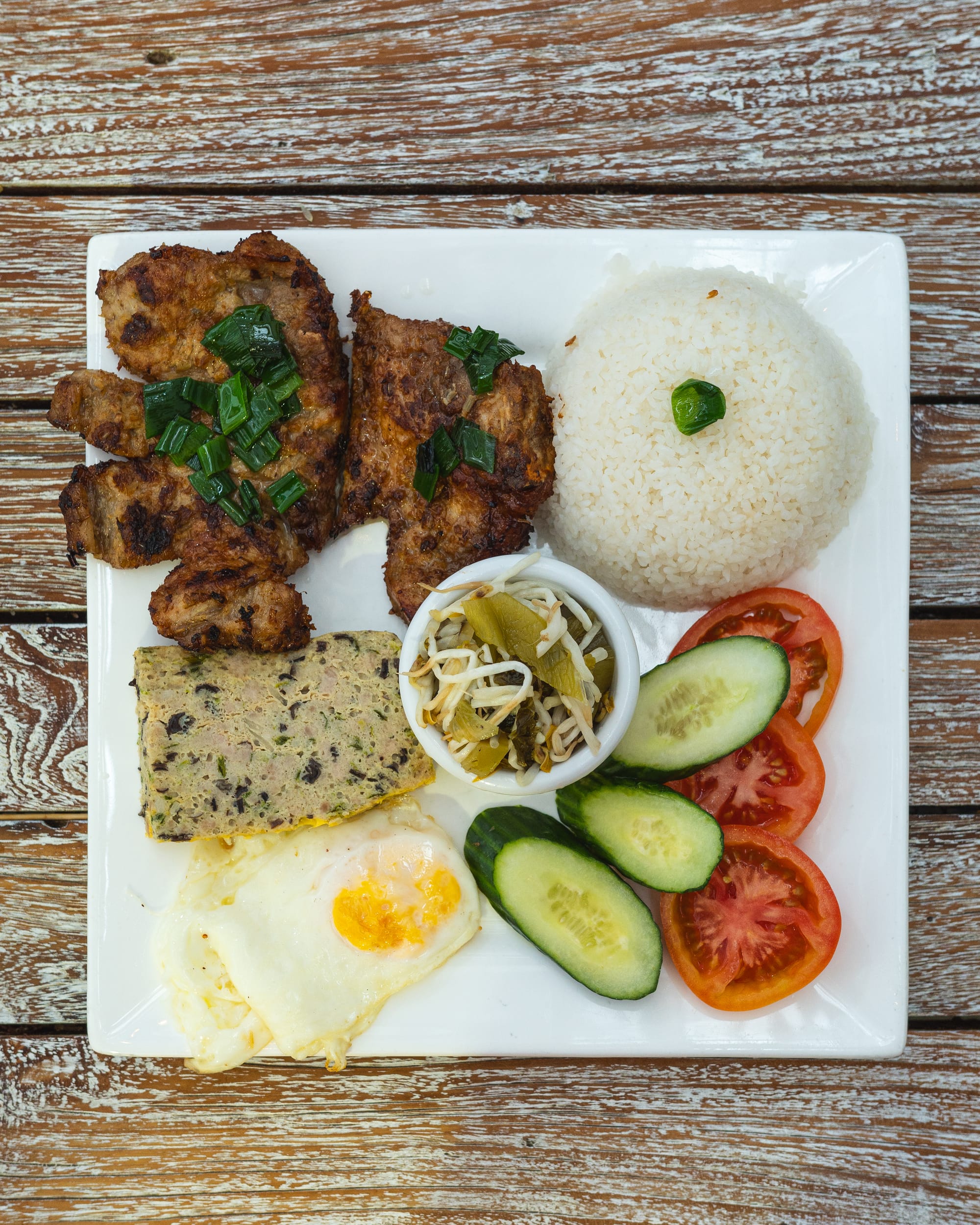 Top down shot of com tam with grilled pork, egg loaf, egg, pickled vegetables, tomato, cucumber and rice
