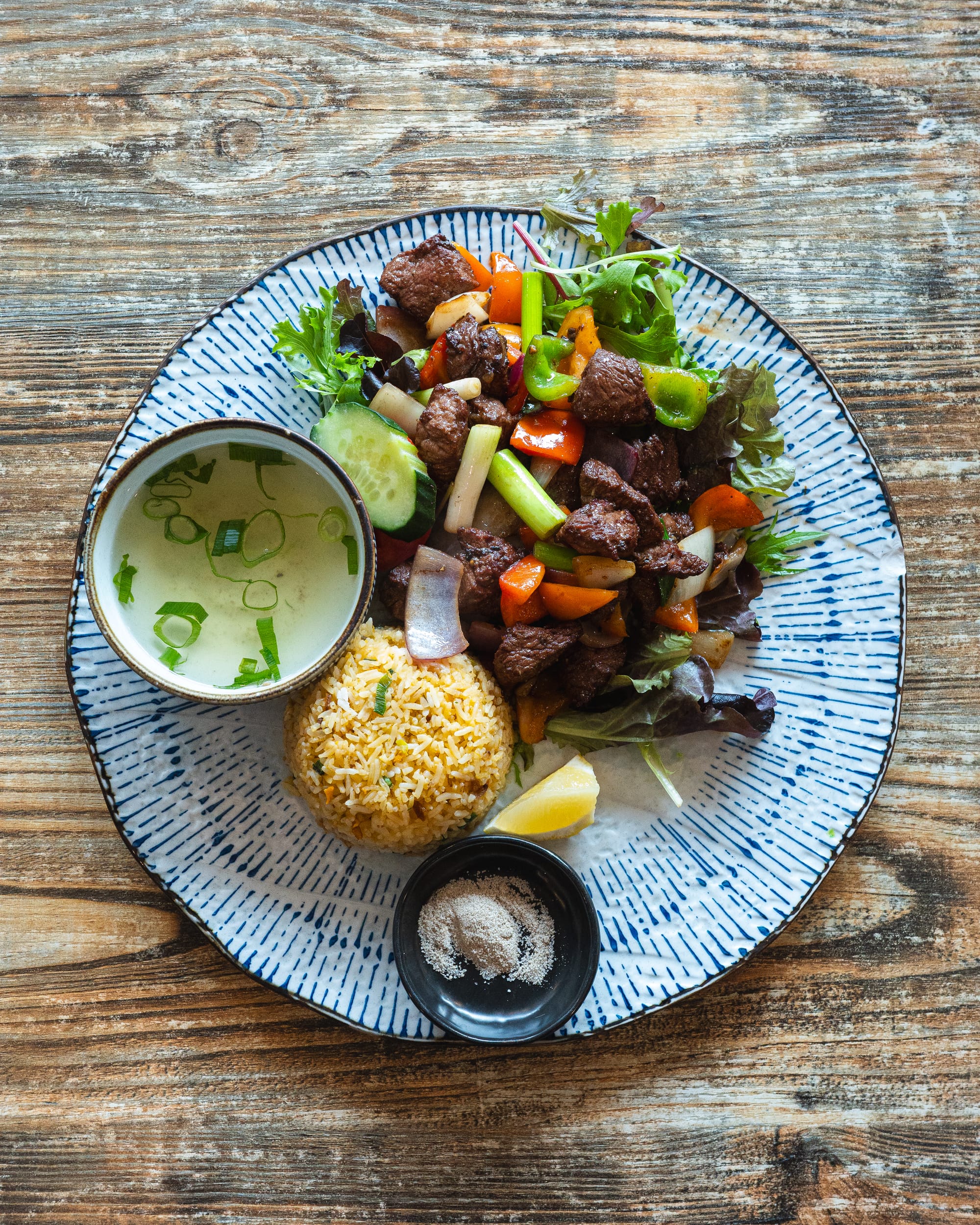 Top down shot of stir fried beef with colourful vegetables, rice and soup