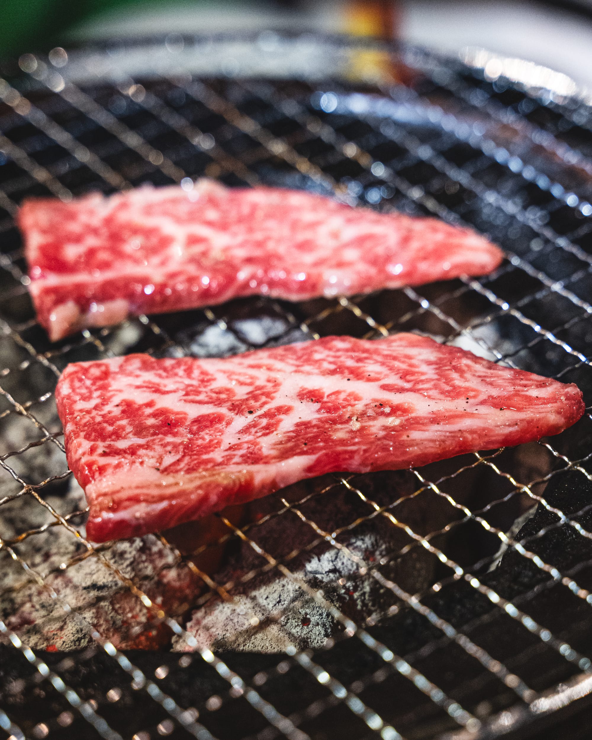 Thinly sliced wagyu sitting on a charcoal grill