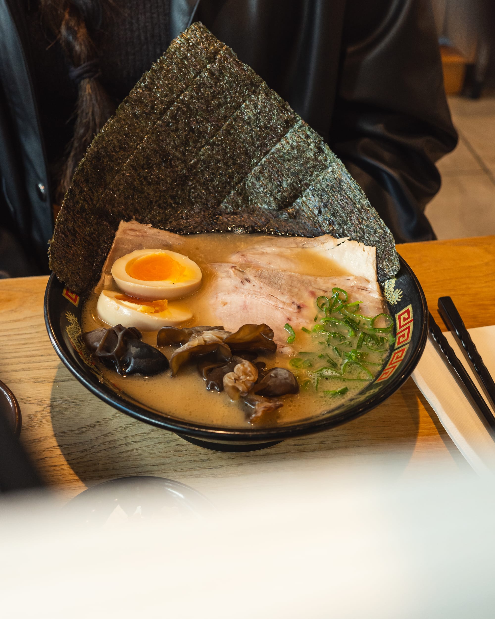 Close up of a bowl of ramen with flavoured egg, mushroom, chashu, seaweed and spring onions showing