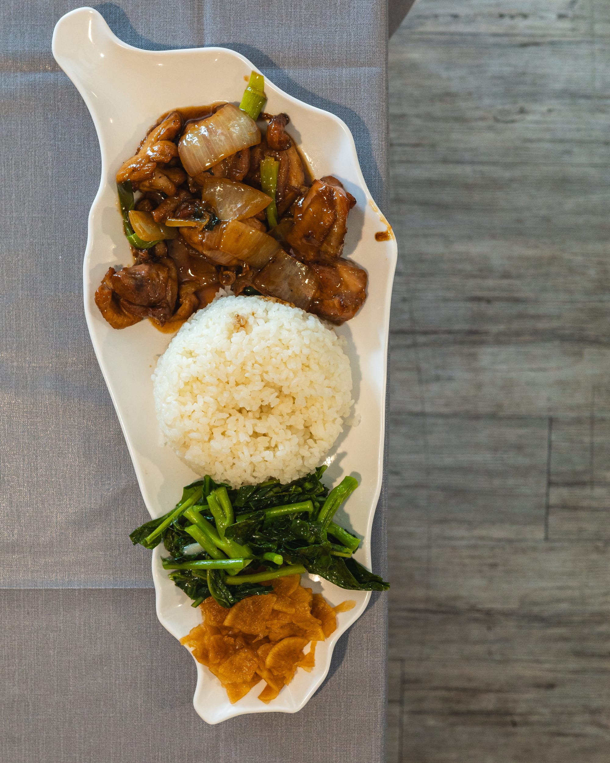 Top down shot of three cup chicken, rice, kai lan and pickled vegetables