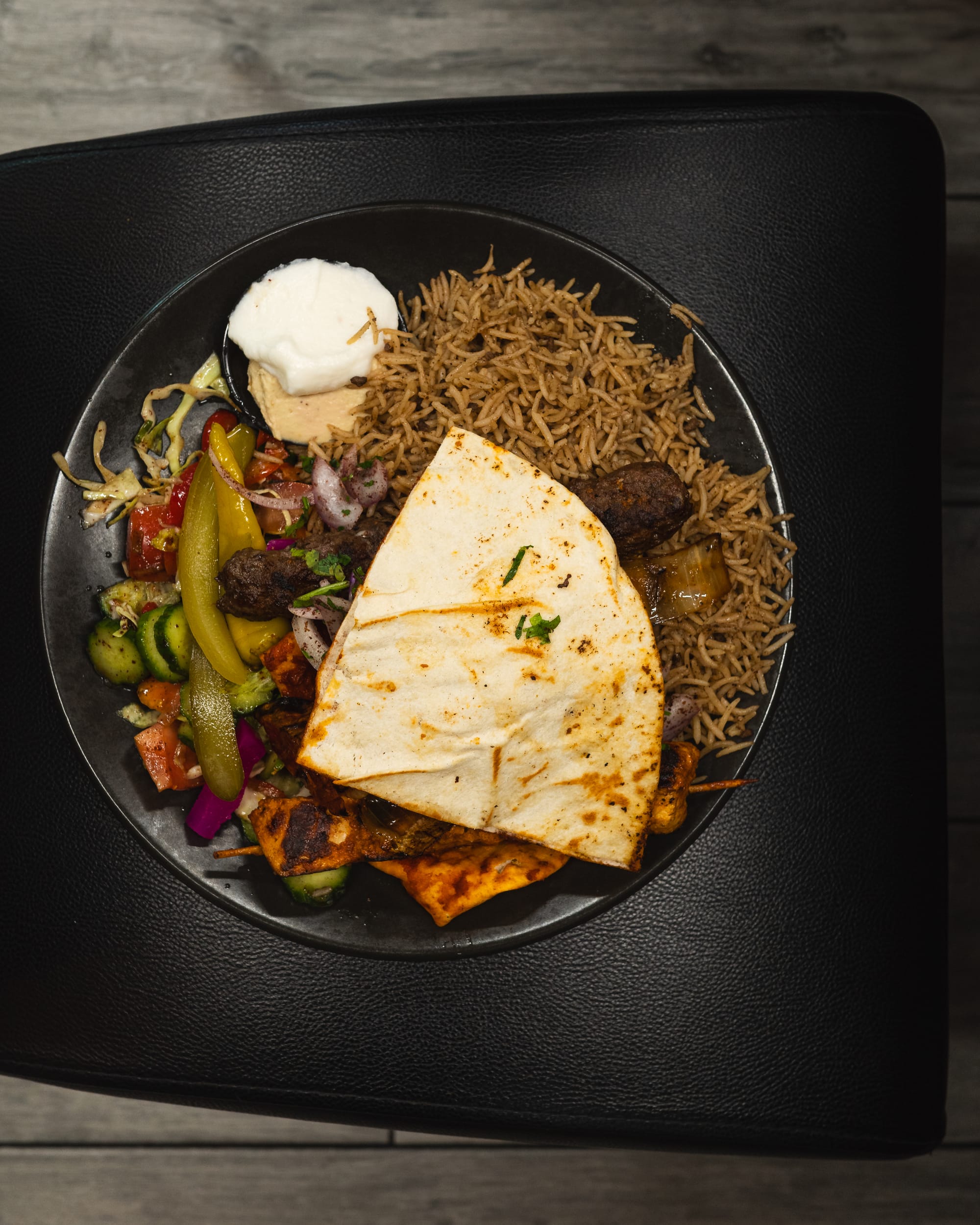 Top down shot of plate with Lebanese bread, rice, garlic sauce, hummus, salad, kofta and skewers