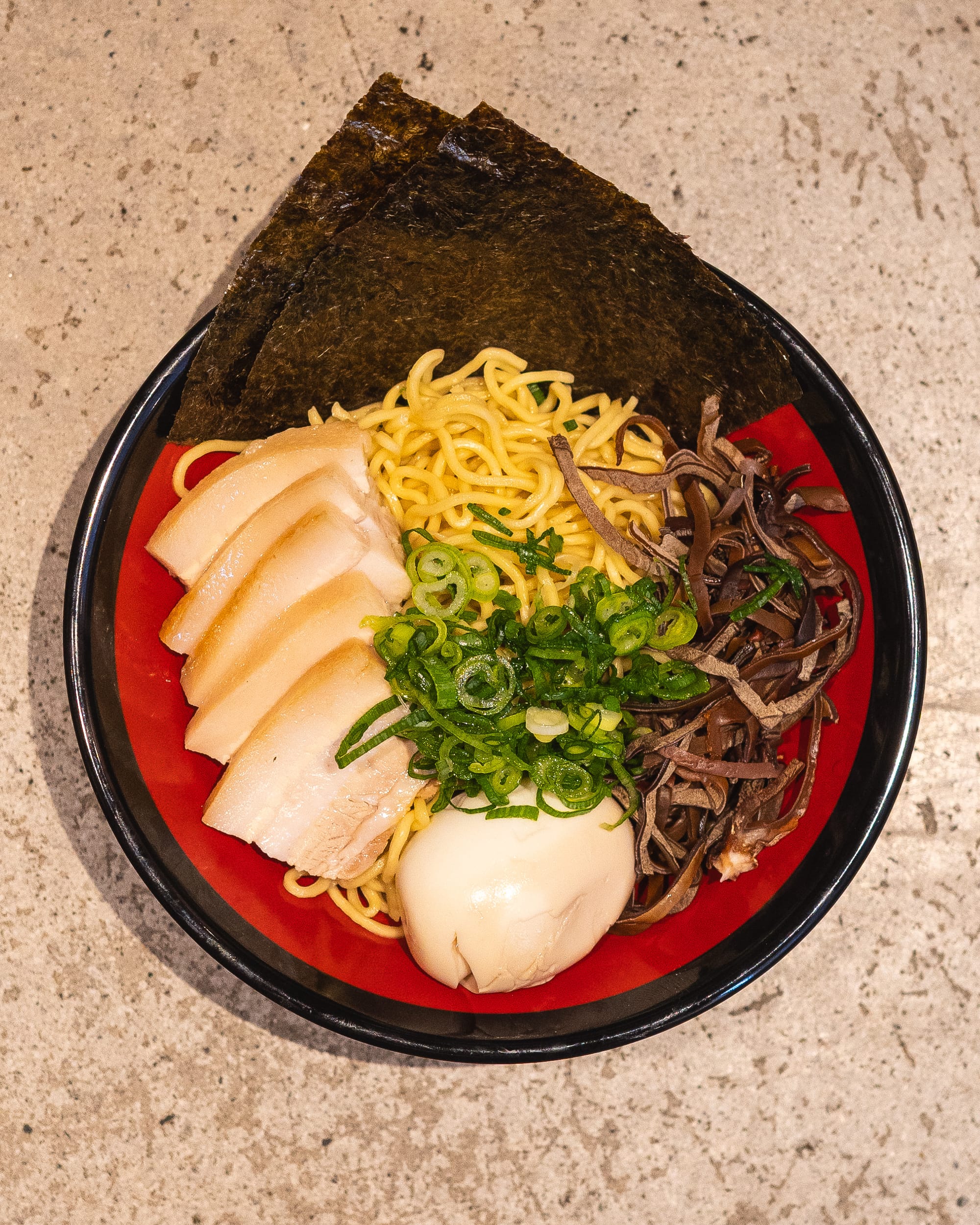 Top down shot of a bowl of ramen with pork chashu, spring onions, black fungus and egg
