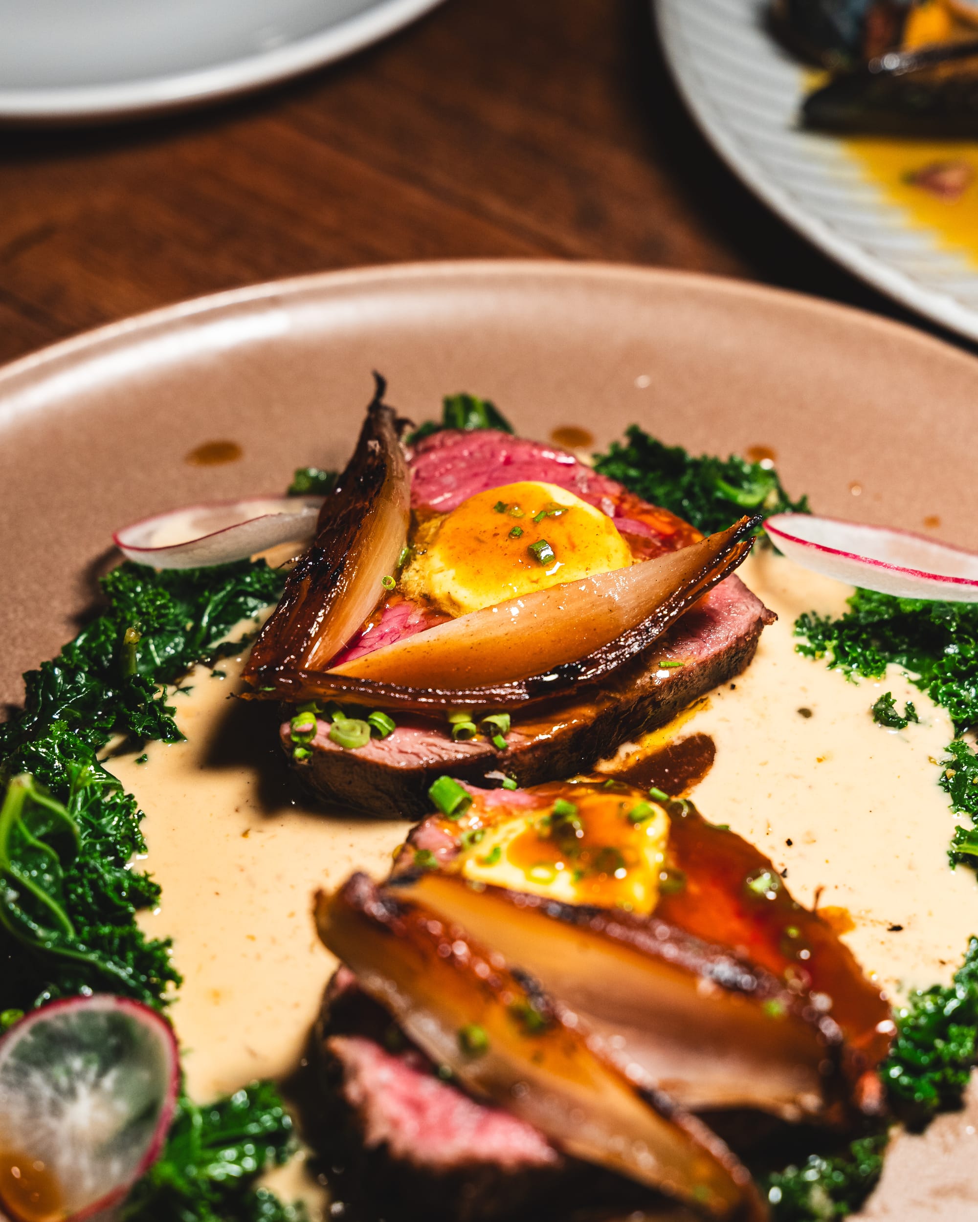 Close up of sliced beef with shallots, kale and peppercorn  sauce