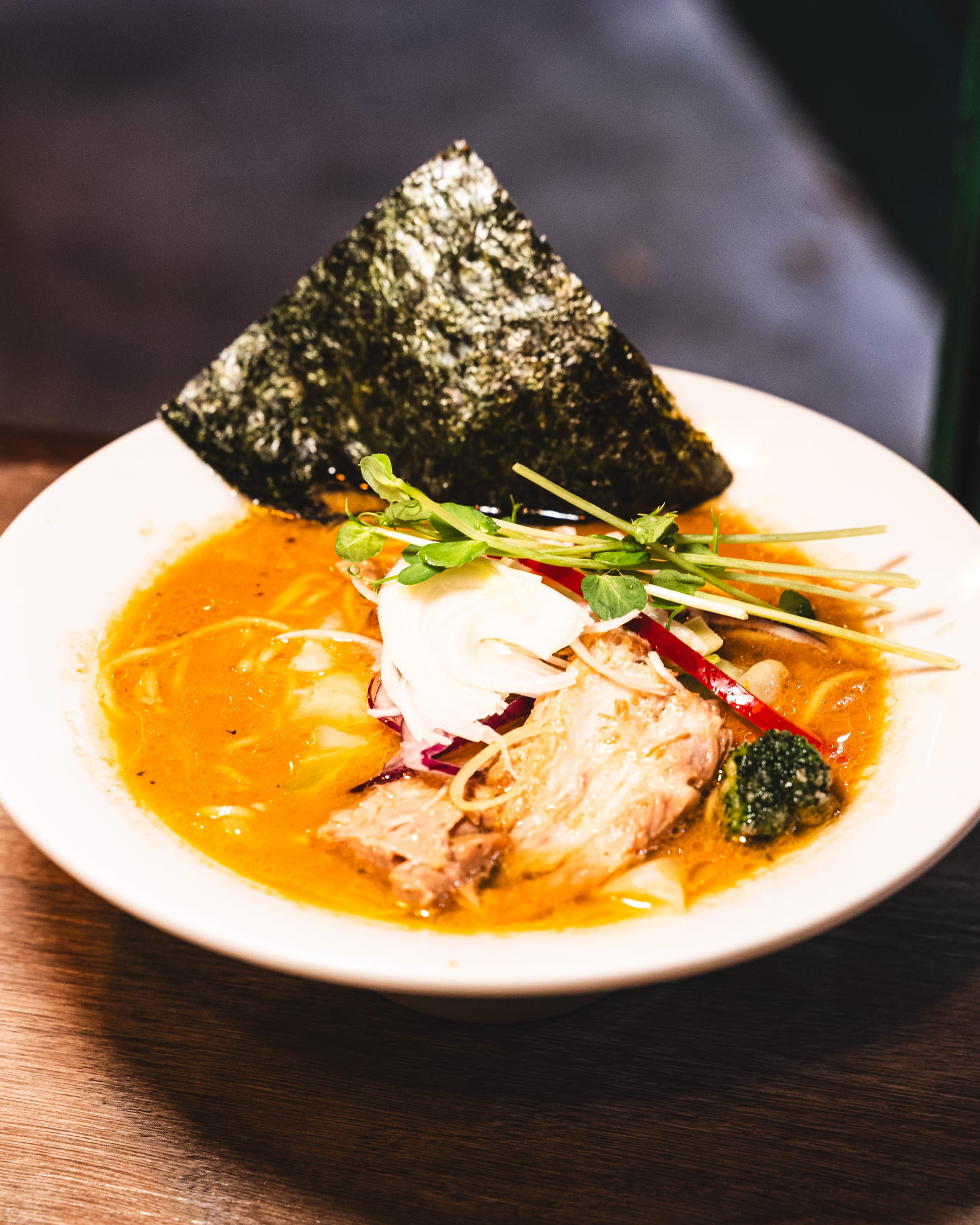 Bowl of ramen with seaweed square, micro vegetables, chicken, capsicum, broccoli
