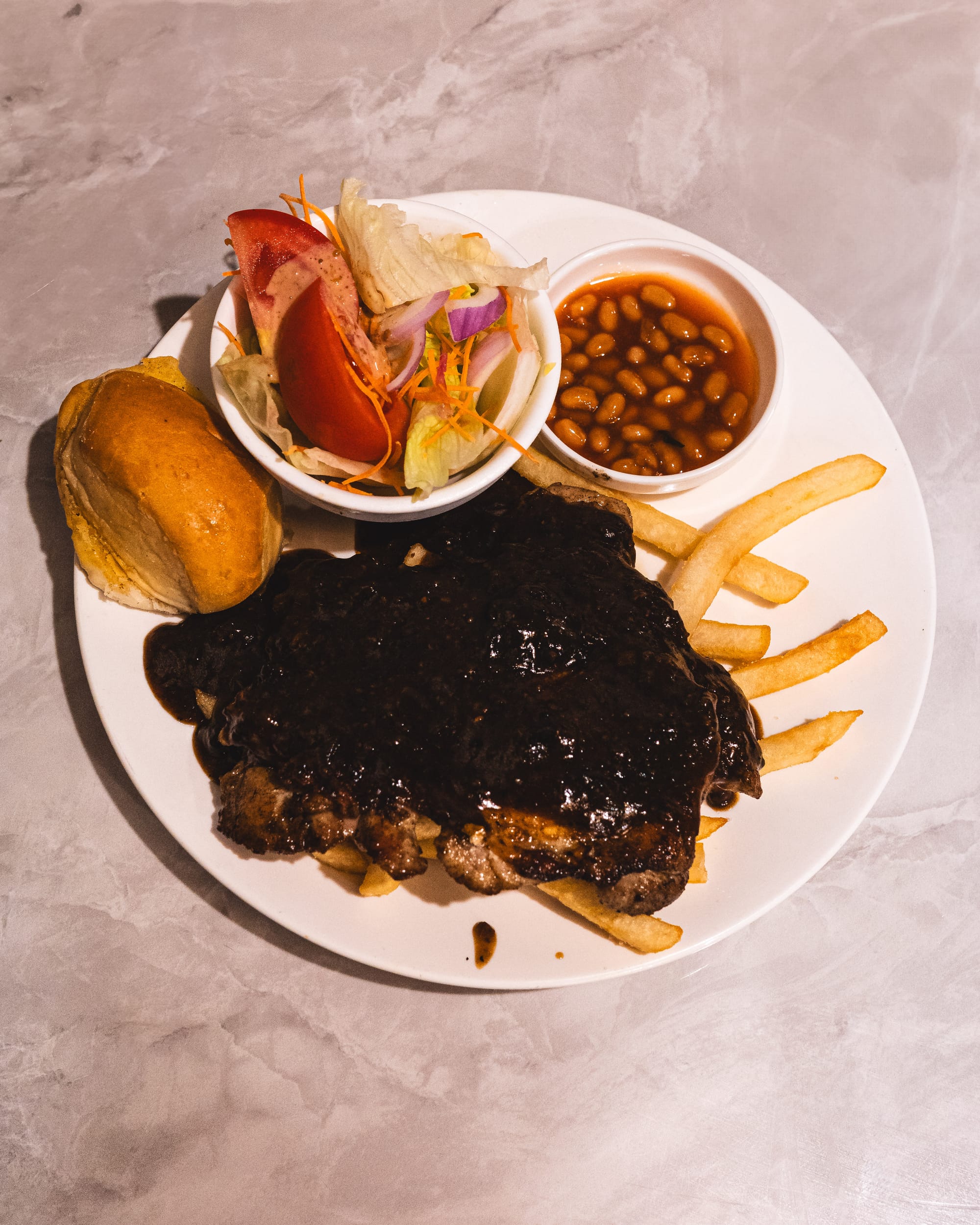 Fried chicken chop with black pepper sauce, bread roll, salad, baked beans and fries