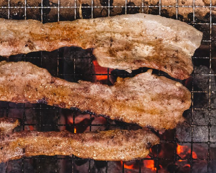 Close up of pork belly grilled on-top of a metal mesh over binchotan charcoal