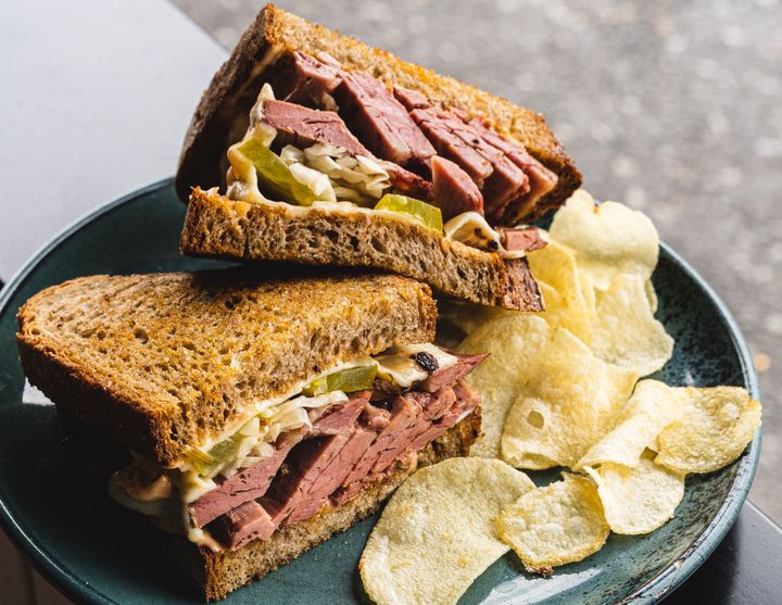 Close up shot of reuben sandwich stacked on-top of each other, with a side of crisps