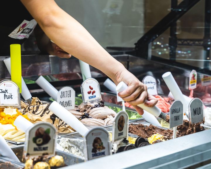 A hand scooping gelato from an ice-cream fridge
