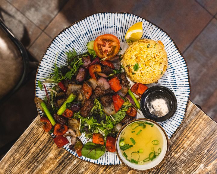 Top down shot of a palte with fried rice, stir fried beef and vegatables, a bowl of soup and a slice of lemon
