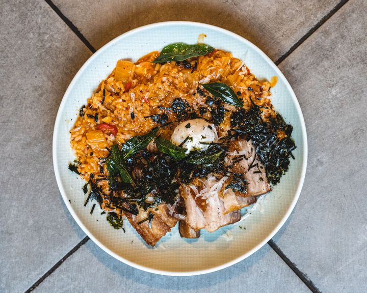 Overhead shot of risotto on a round plate with a poached egg and crispy pork belly