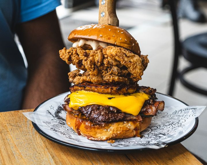 Large burger with fried chicken, melted cheese and bacon with a steak knife holding it together
