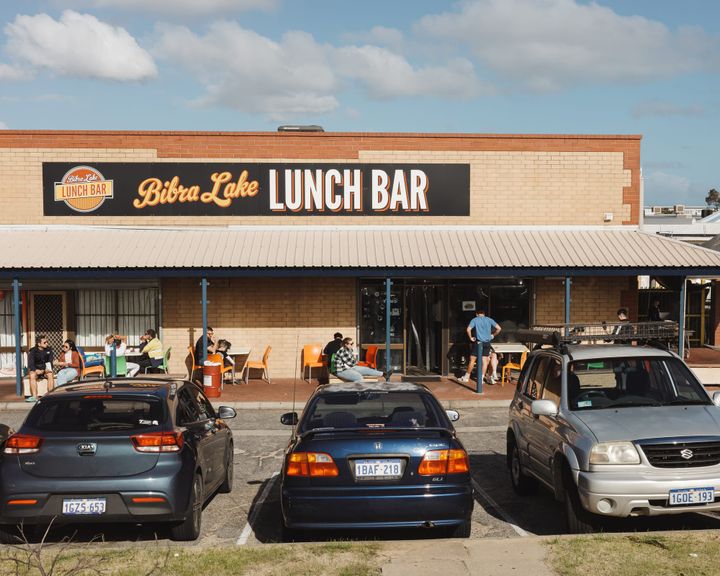 Exterior of Bibra Lake Lunch Bar showing people dining outside and parked cars
