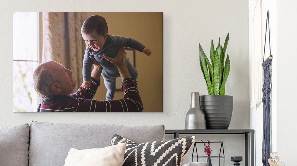 A canvas print of a grandfather holding up a child and hanging over a couch