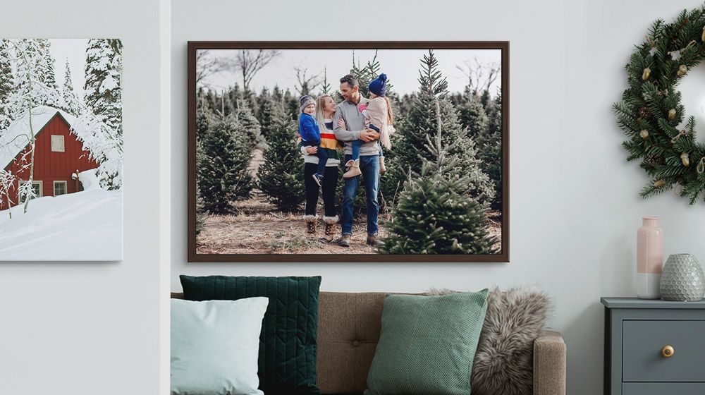 A framed canvas print of a family at a Christmas tree farm hanging over a sofa