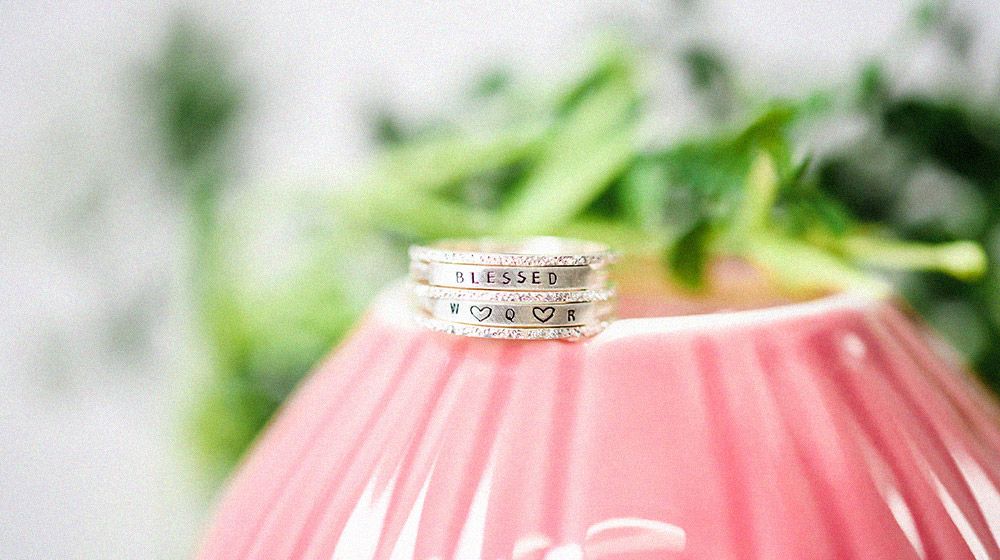 a pair of personalized diamond rings sitting on pink planter with green plant