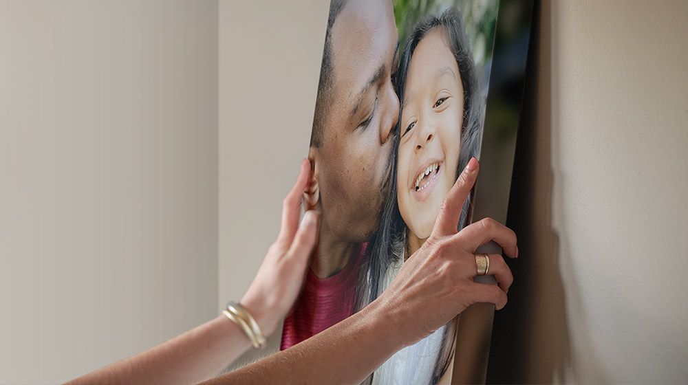 a woman hanging a canvas of a black dad and mixed daughter
