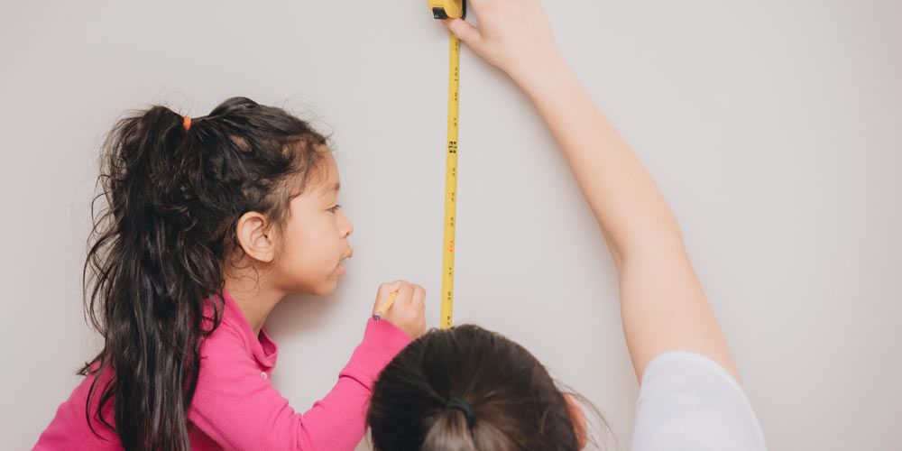 woman measuring empty wall space while young girl marks hanging spot with pencil