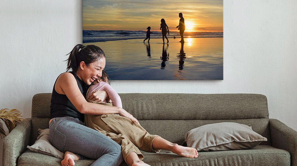 A mother and child embrace on a couch in front of a large canvas print of the beach.