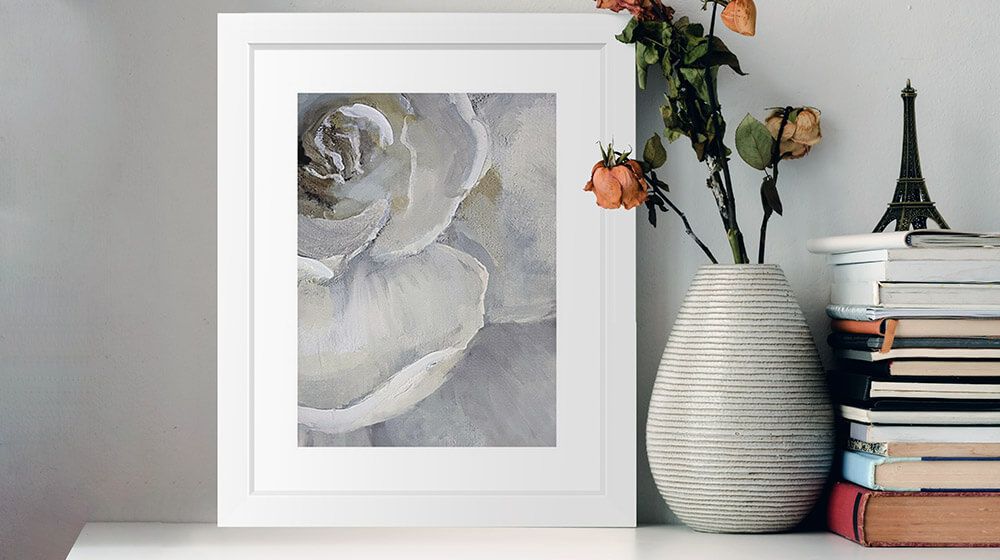 A framed print of a floral art piece sitting on a shelf next to some books