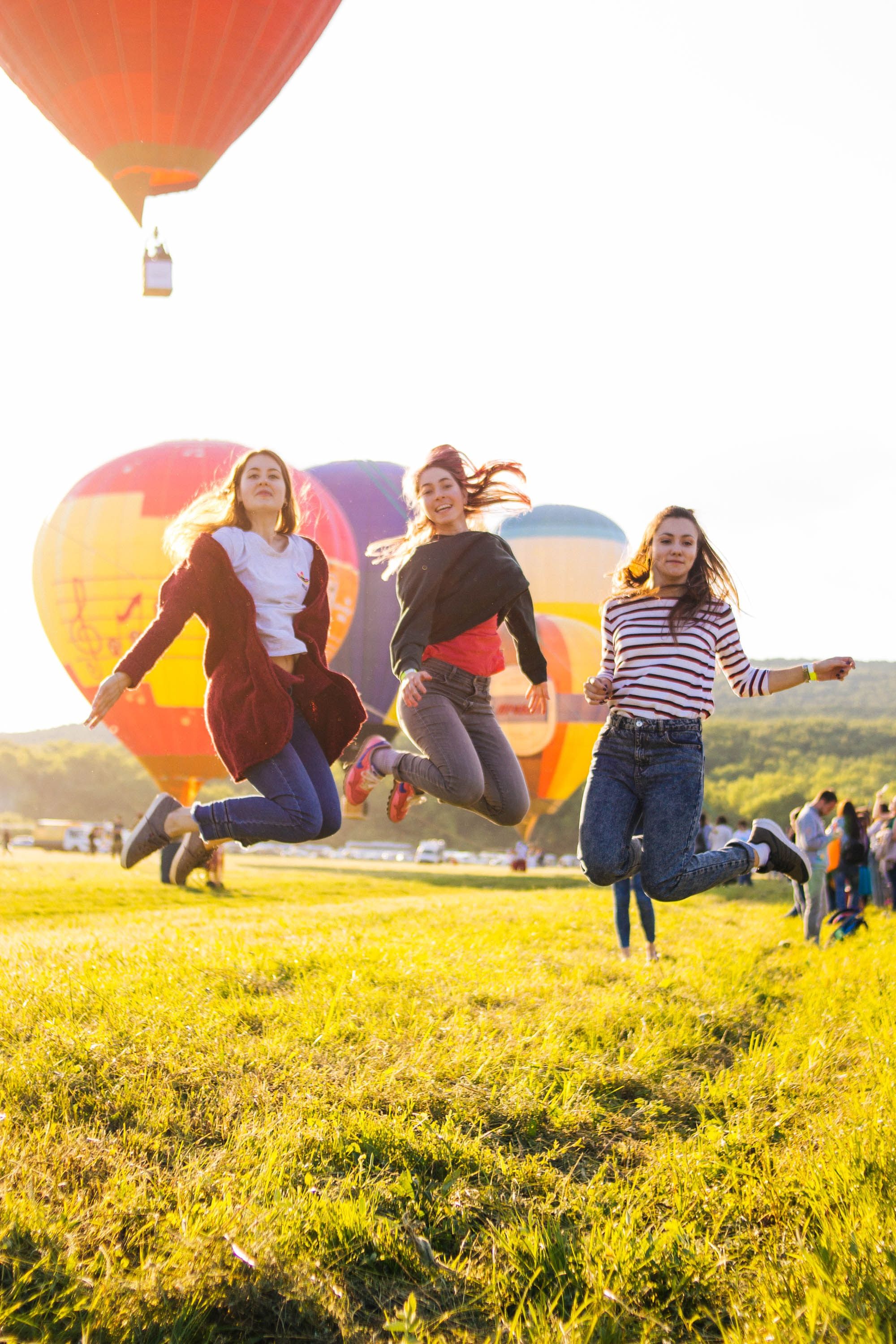 Three women jumping in mid-pose for a photoshoot at a balloon festival