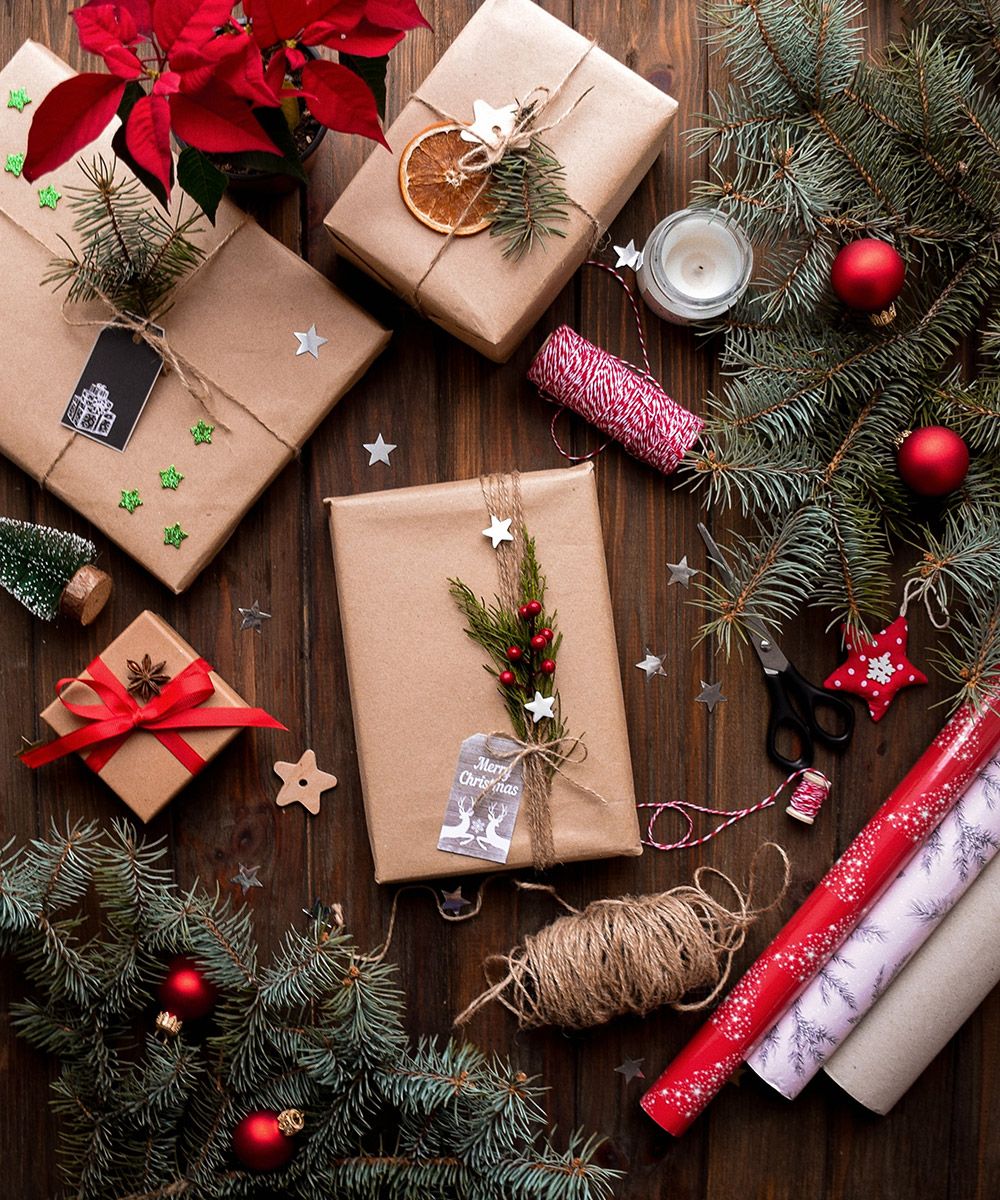 Holiday packages sitting next to trees with ornaments and holiday wrapping paper