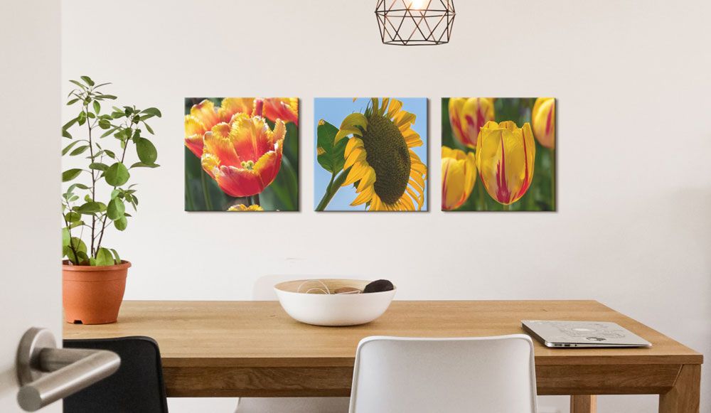 A simple and rustic wooden table sits in front of a wall, which displays three canvas prints of color and bright spring flowers.