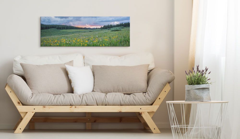 A canvas print of a scenic pasture hangs on a wall in a bohemian and simplistic living room