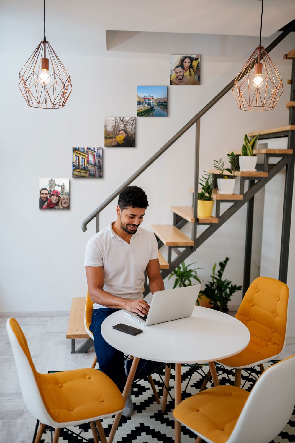 Man on his computer sitting down in a modern basement with canvas prints hanging on a wall along the staircase