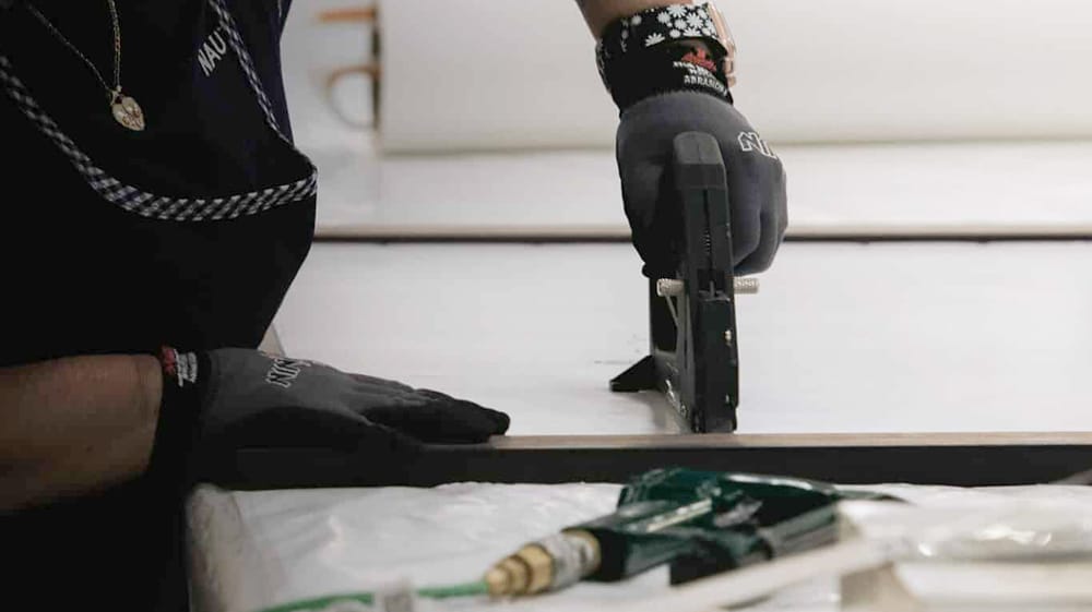 Hands carefully stretching and stapling canvas over frame, emphasizing craftsmanship and attention to detail in production
