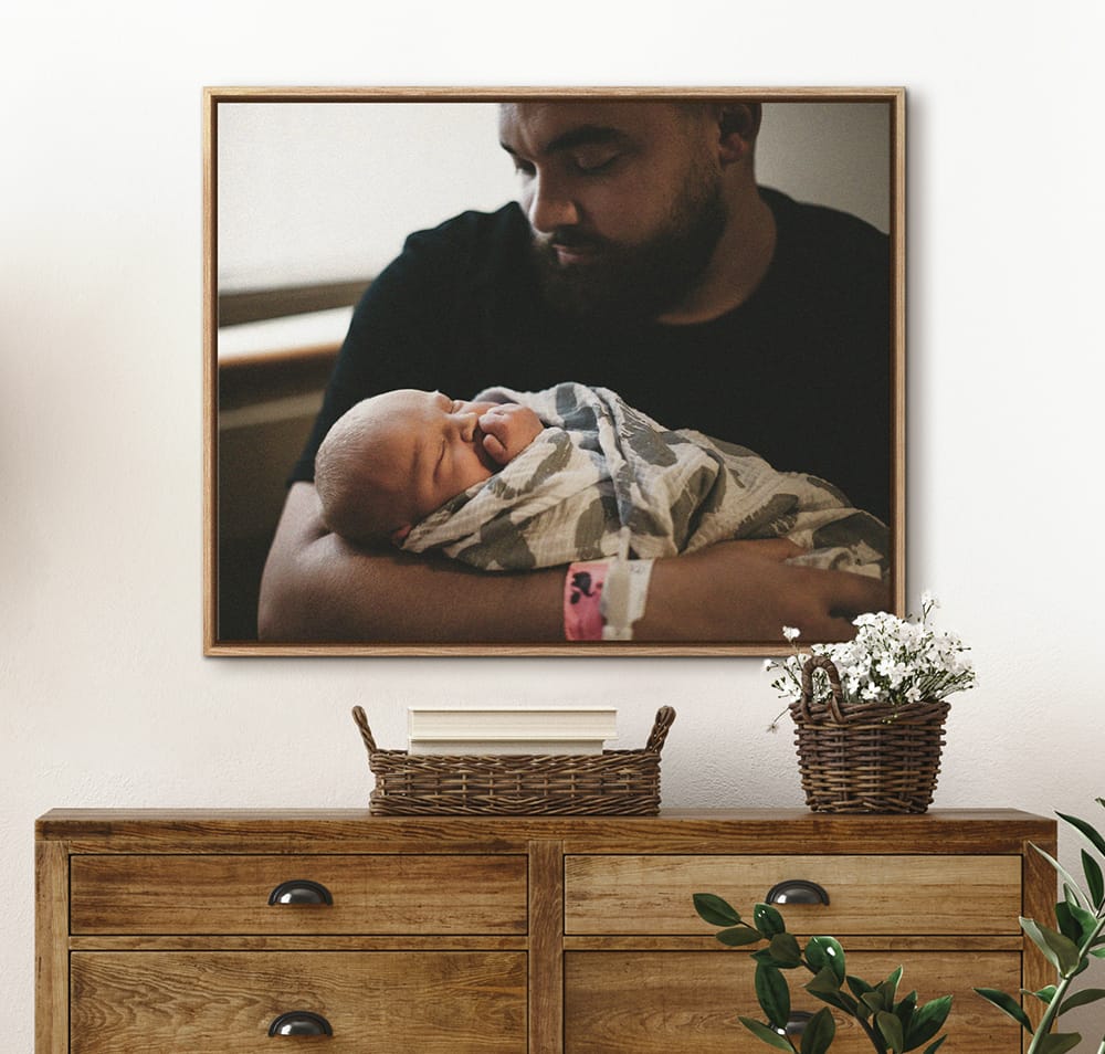 Floating frame canvas print of a newborn moment displayed above a dresser in a home