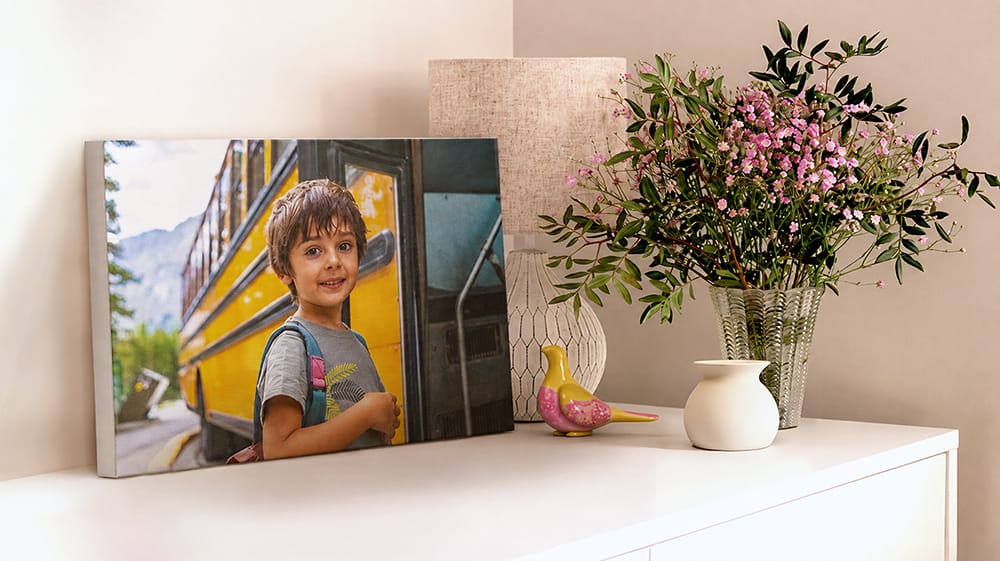 A canvas print of a smiling boy with a backpack beside a yellow school bus rests on a white cabinet.