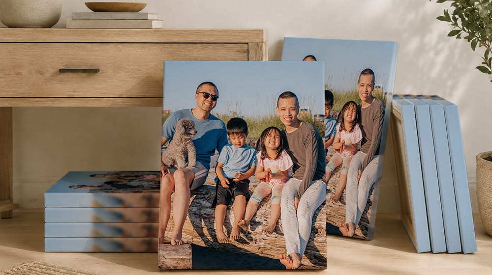 Ten canvas prints with blur edges featuring the same family beach portrait with a dog, stacked and propped beside a wooden cabinet.
