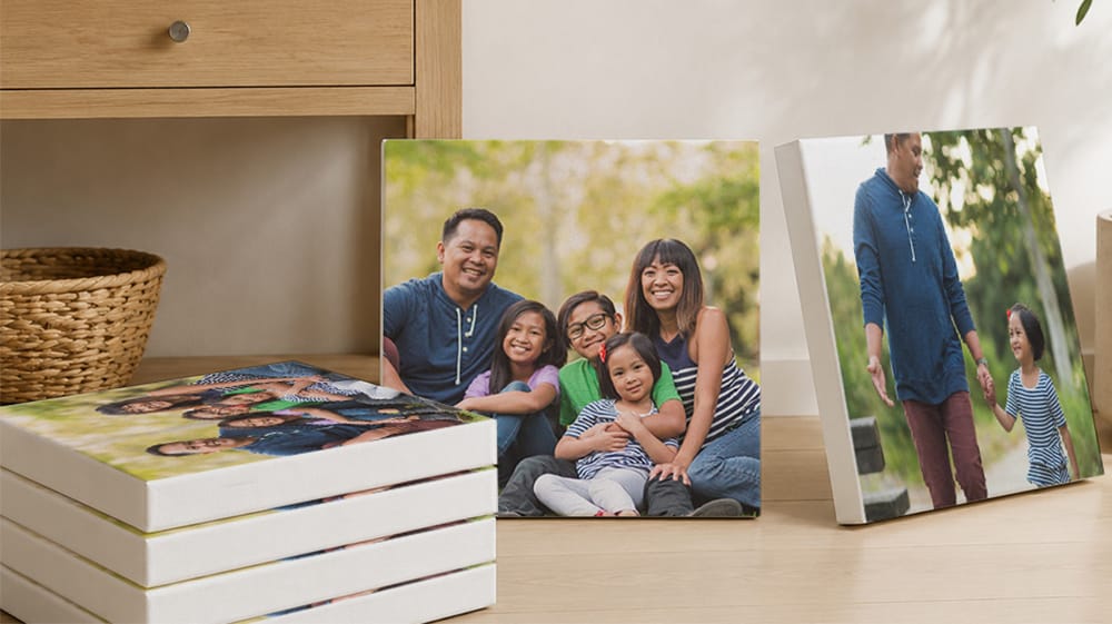 Same-size family photo canvas prints stacked and propped beside a wooden cabinet, ready to give as gifts.