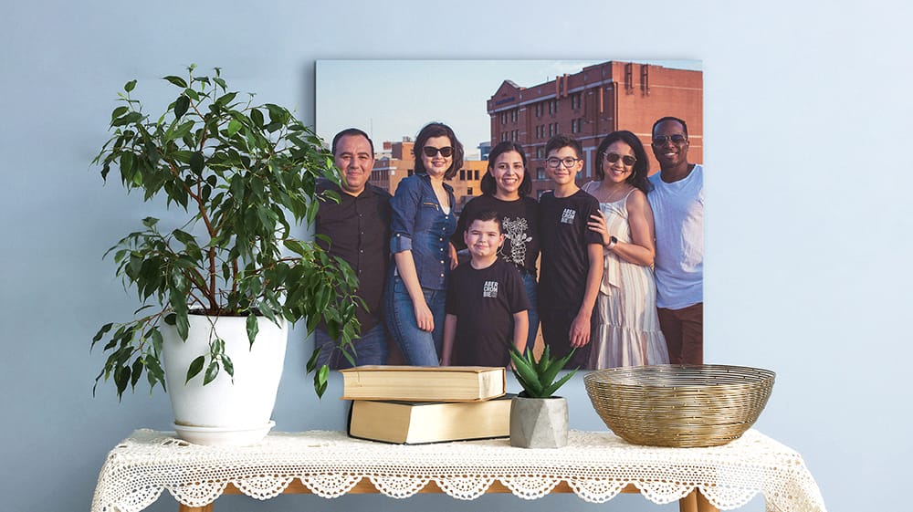 Family vacation photo on canvas displayed above a table with plants, books and a woven basket.