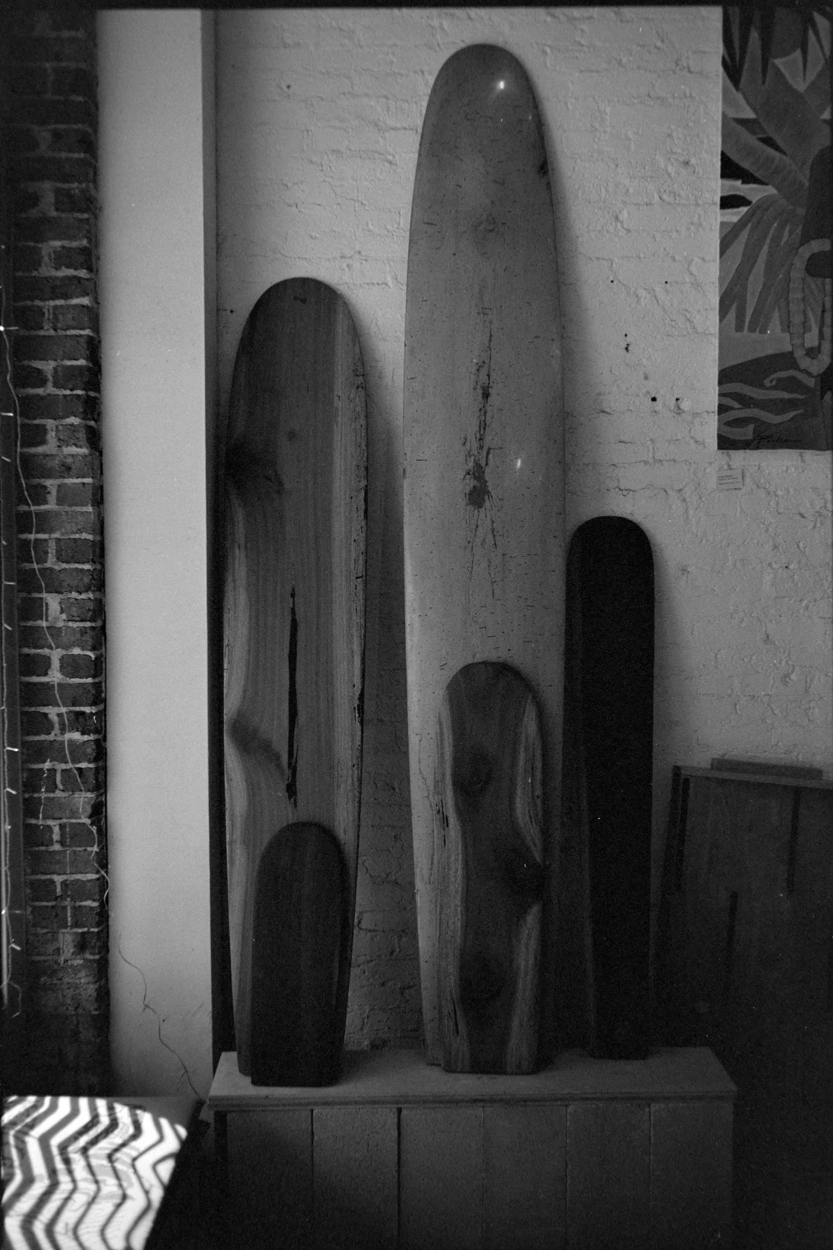 A black and white image of several wooden surfboards stacked against a white wall.