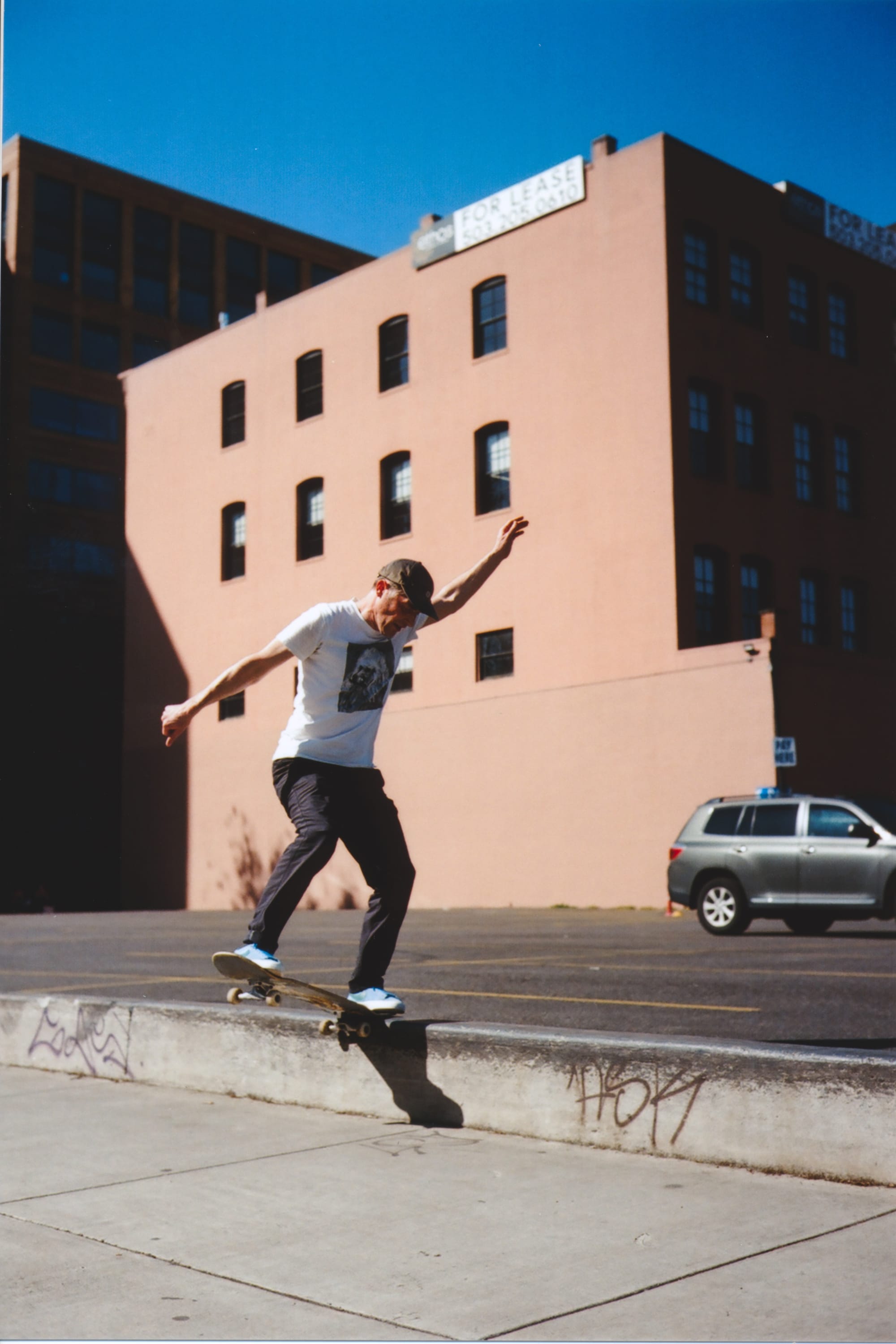 A regular footed skateboarder nosesliding to the right and the background is a pink building.