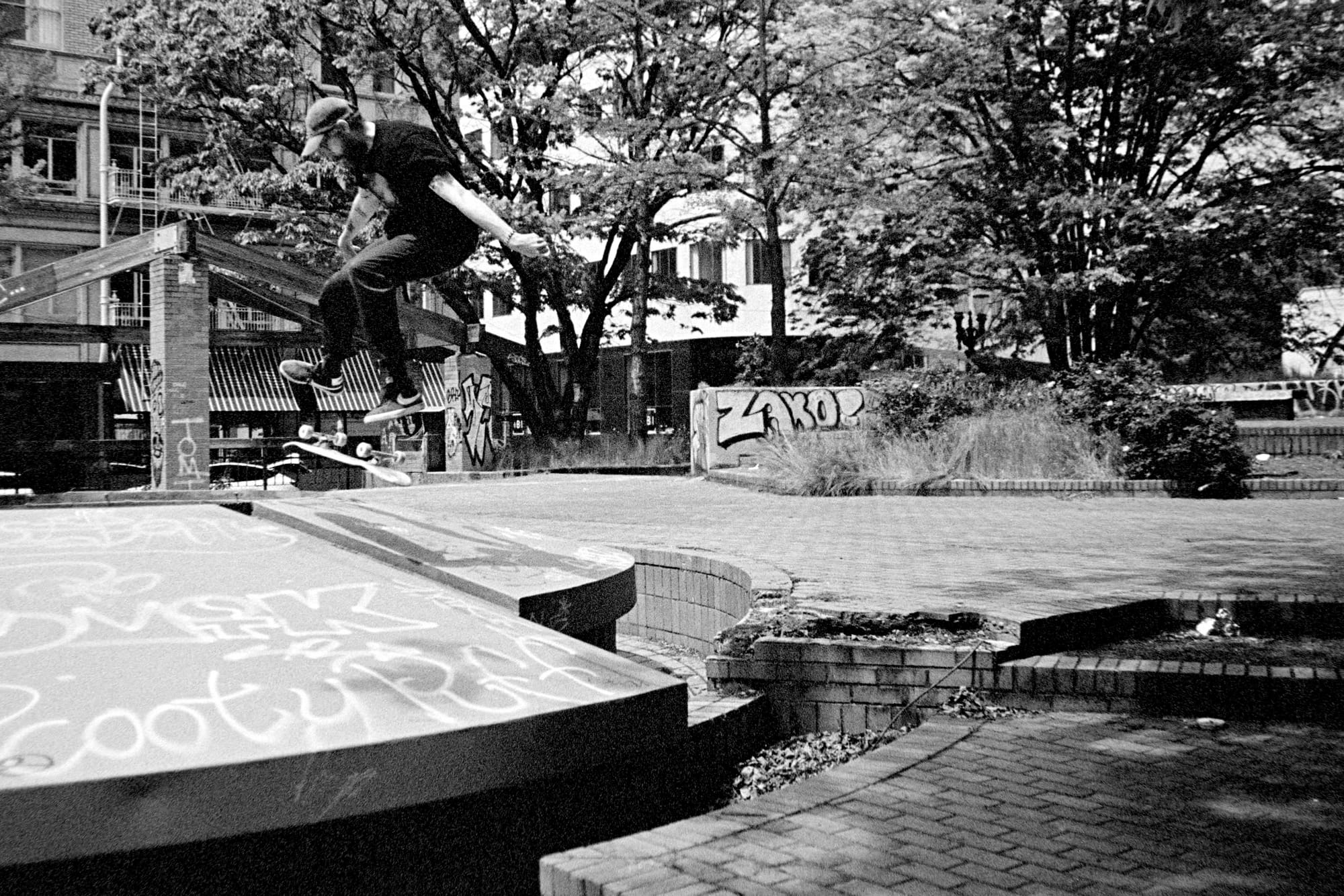 A skater doing a kickflip on a metal fountain in the middle of a brick plaza.