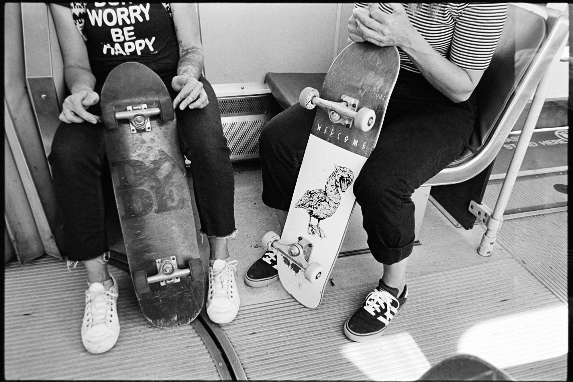 2 women holding sitting on a train holding their skateboards.