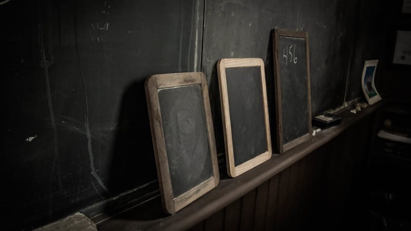 Three small chalkboards lean up against a larger chalkboard, at an artful angle. All are empty of text, except one that bears simply “456”.