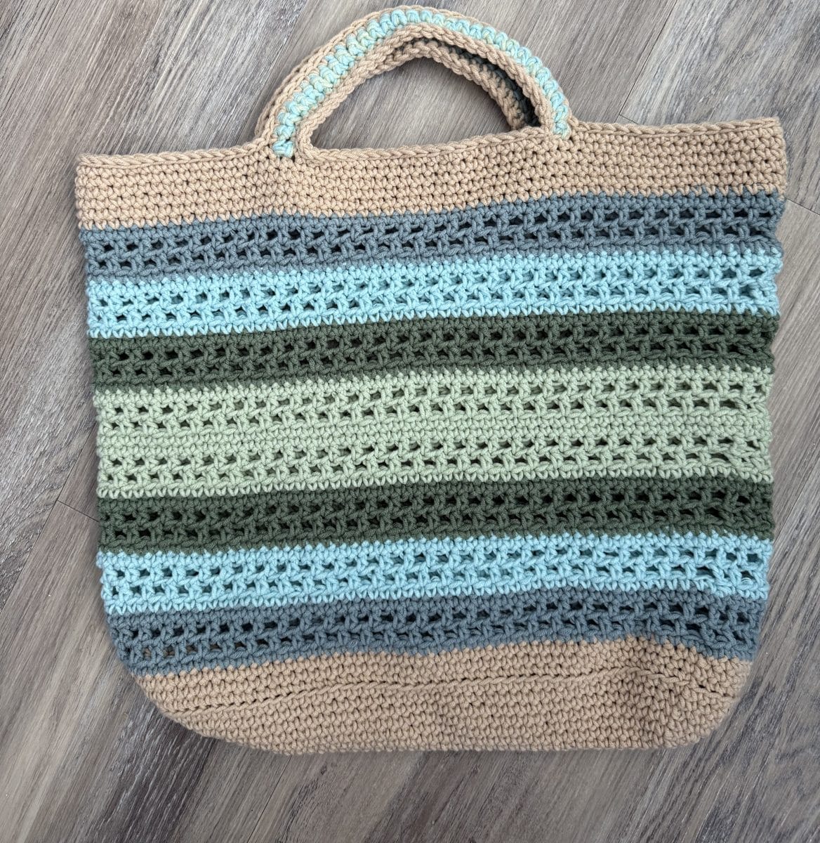 A handmade crochet market tote in sand, slate blue, aqua, olive, and sage stripes