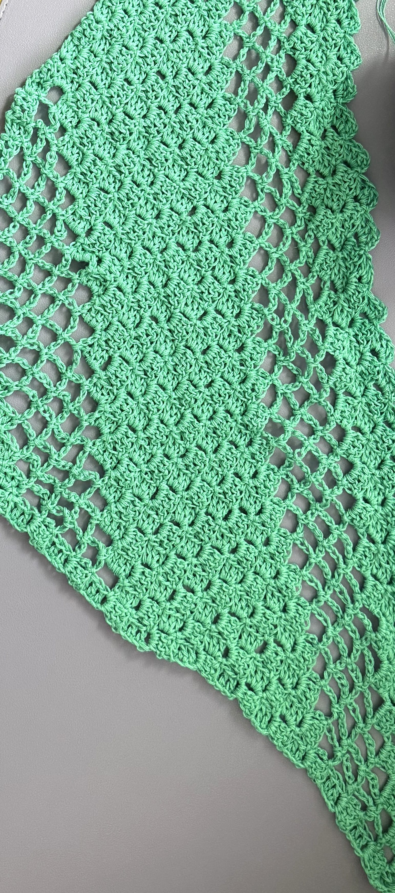 A green lace crochet shawl in progress on a lilac mat