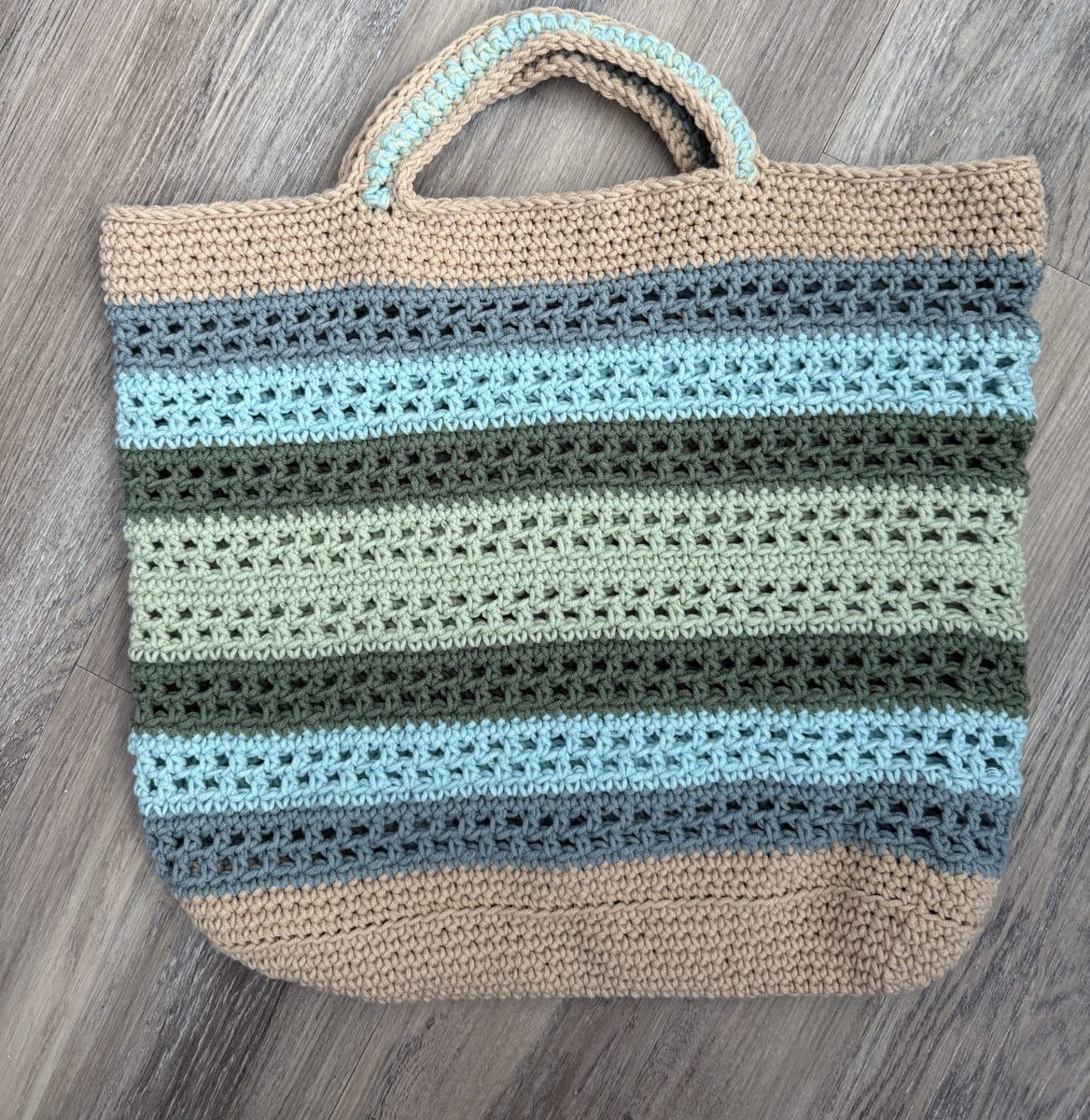 The Coastline Tote, a striped crochet beach bag, on a wood floor
