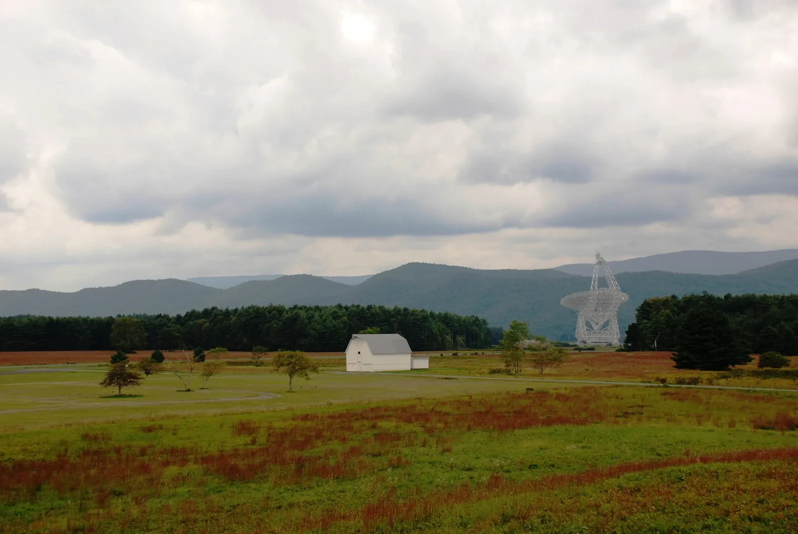 The Green Bank Telescope rises above a green field with wooded mountains behind it.