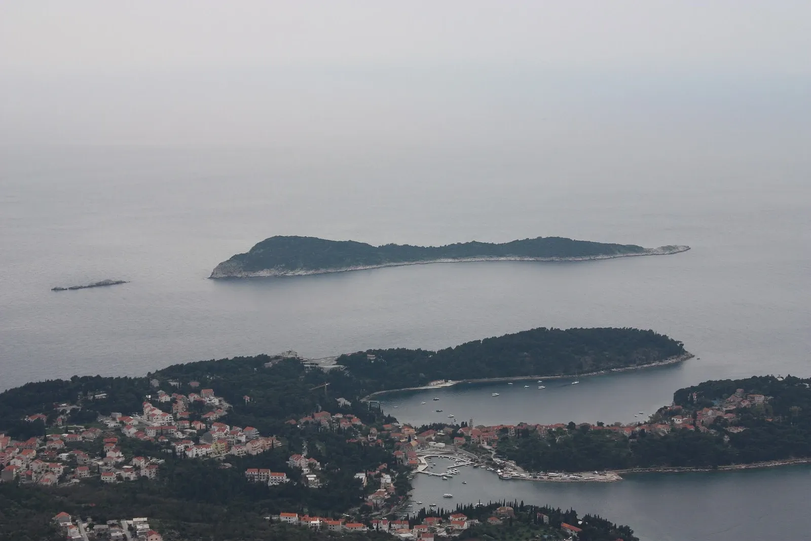 Mrkan island beyond Cavtat’s shore and harbor, with a band of open sea between them.