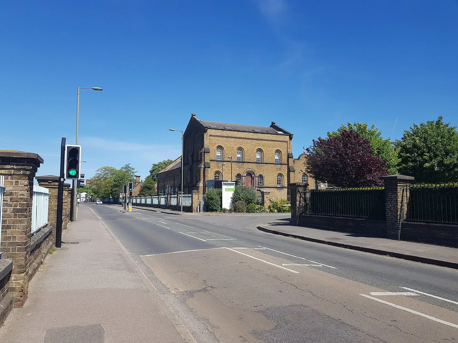 A surviving brick waterworks building at Seething Wells beside a modern road and trees.