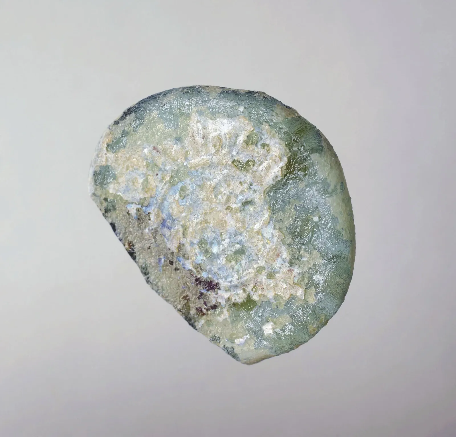 A pale green glass weight with a weathered stamped face